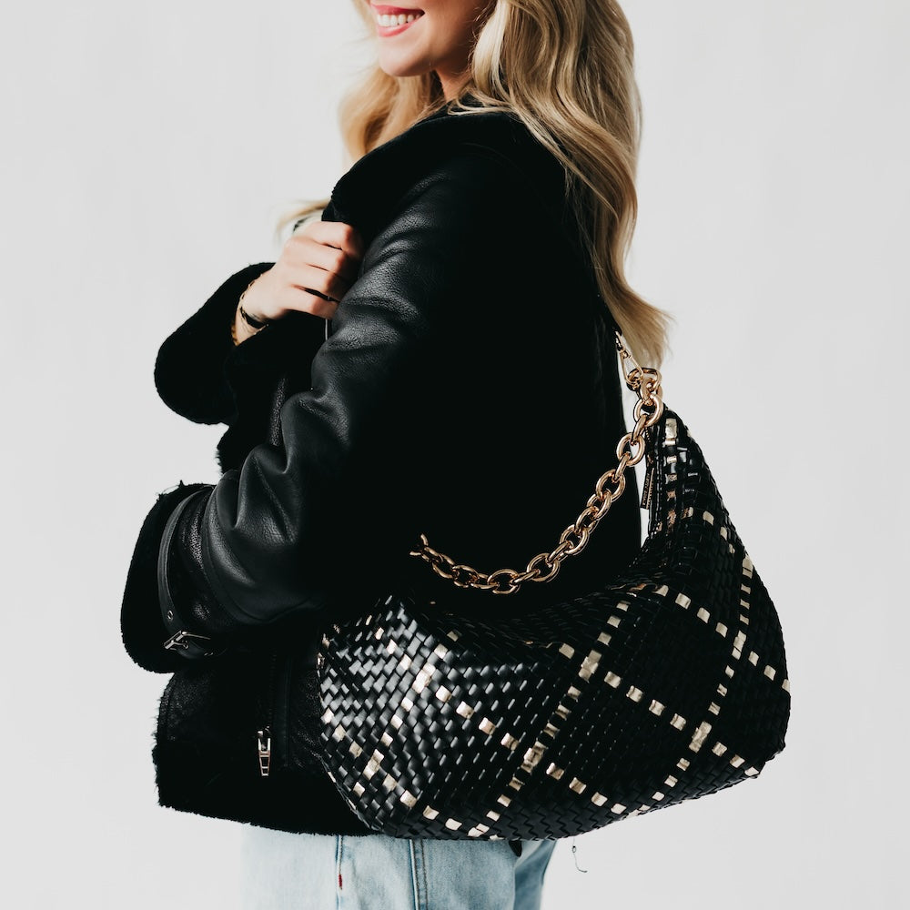 Person holding a black woven handbag with a gold chain strap against a light background