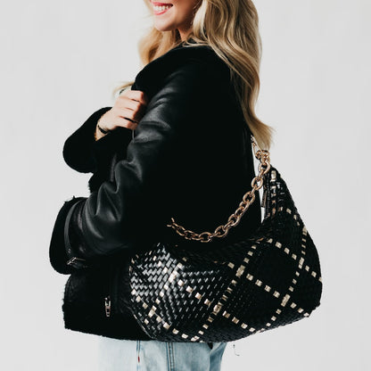 Person holding a black woven handbag with a gold chain strap against a light background