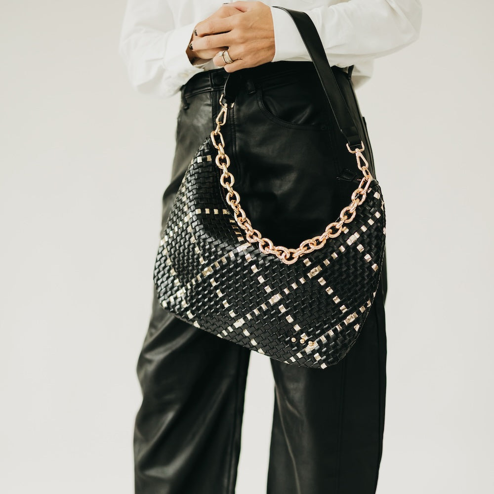 Black woven handbag with gold chain detail held by a person wearing a white shirt and black pants.
