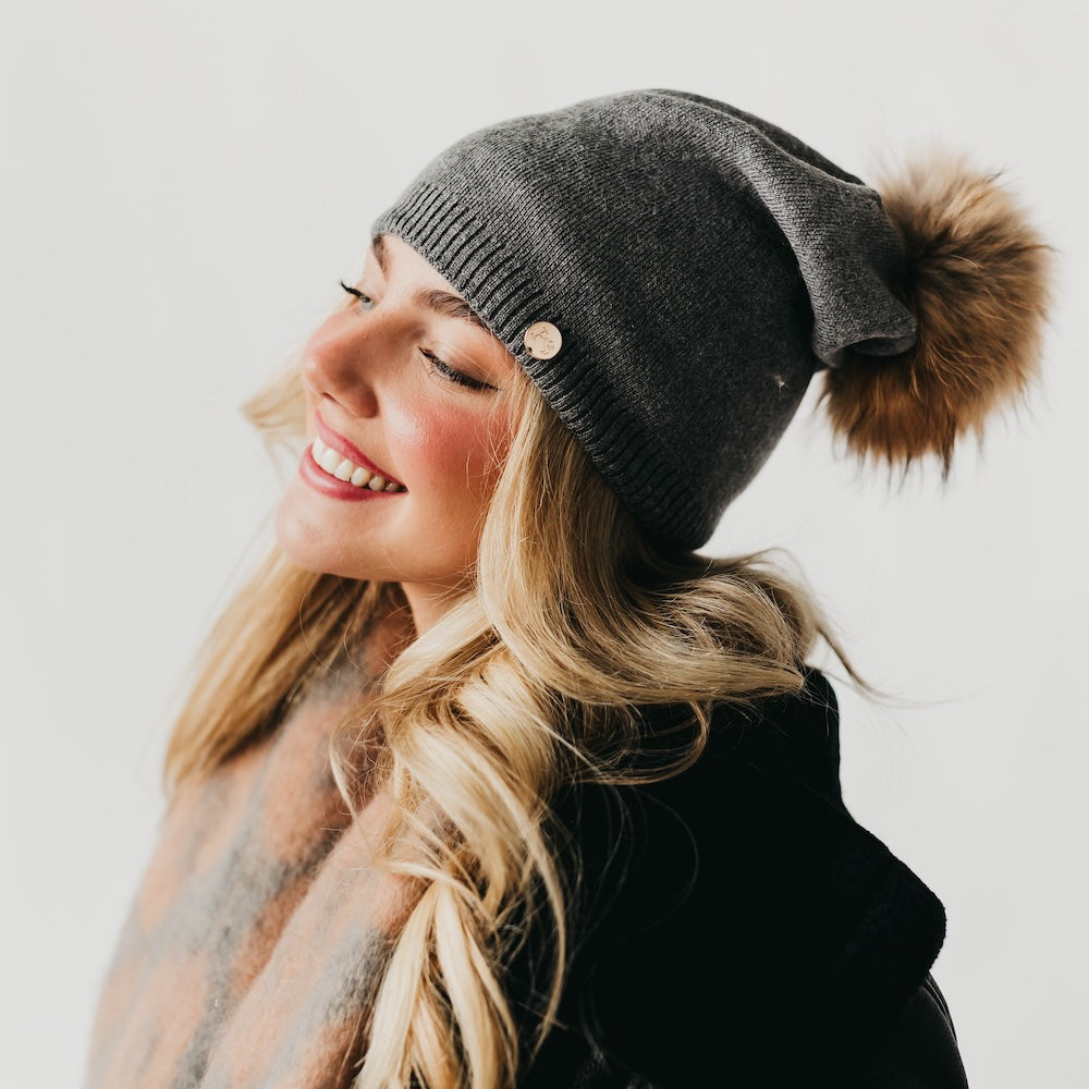 Woman wearing a gray knit beanie with a pom-pom on a plain background
