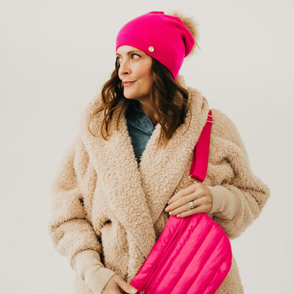 Woman wearing a pink beanie and holding a pink bag against a white background