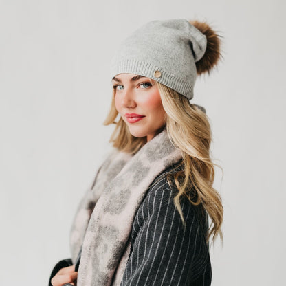 Woman wearing a gray knit beanie with a pom-pom and a scarf against a white background