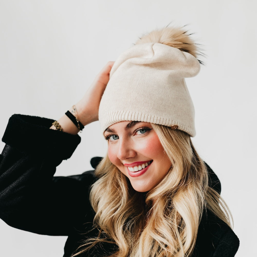 Woman wearing a beige beanie with a pom-pom on a white background