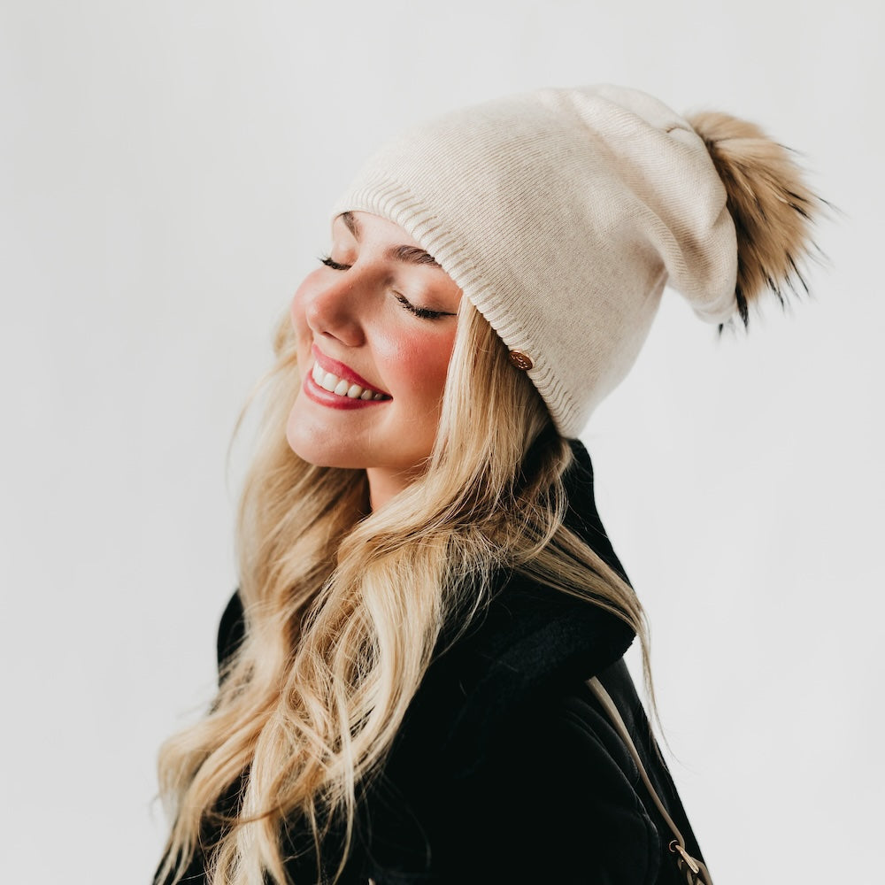 Woman wearing a beige beanie with a pom-pom on a plain background