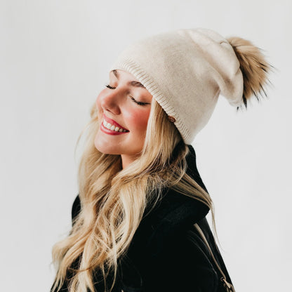 Woman wearing a beige beanie with a pom-pom on a plain background