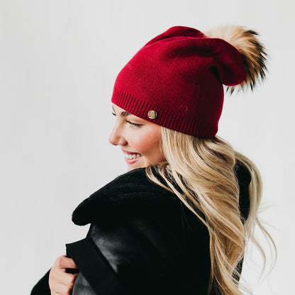 Woman wearing a red beanie with a pom-pom on a plain background