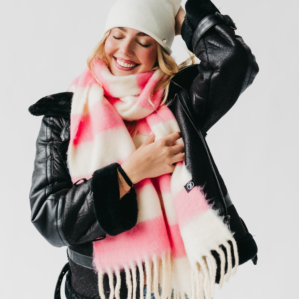 Woman wearing a pink and white scarf with a black leather jacket on a light gray background