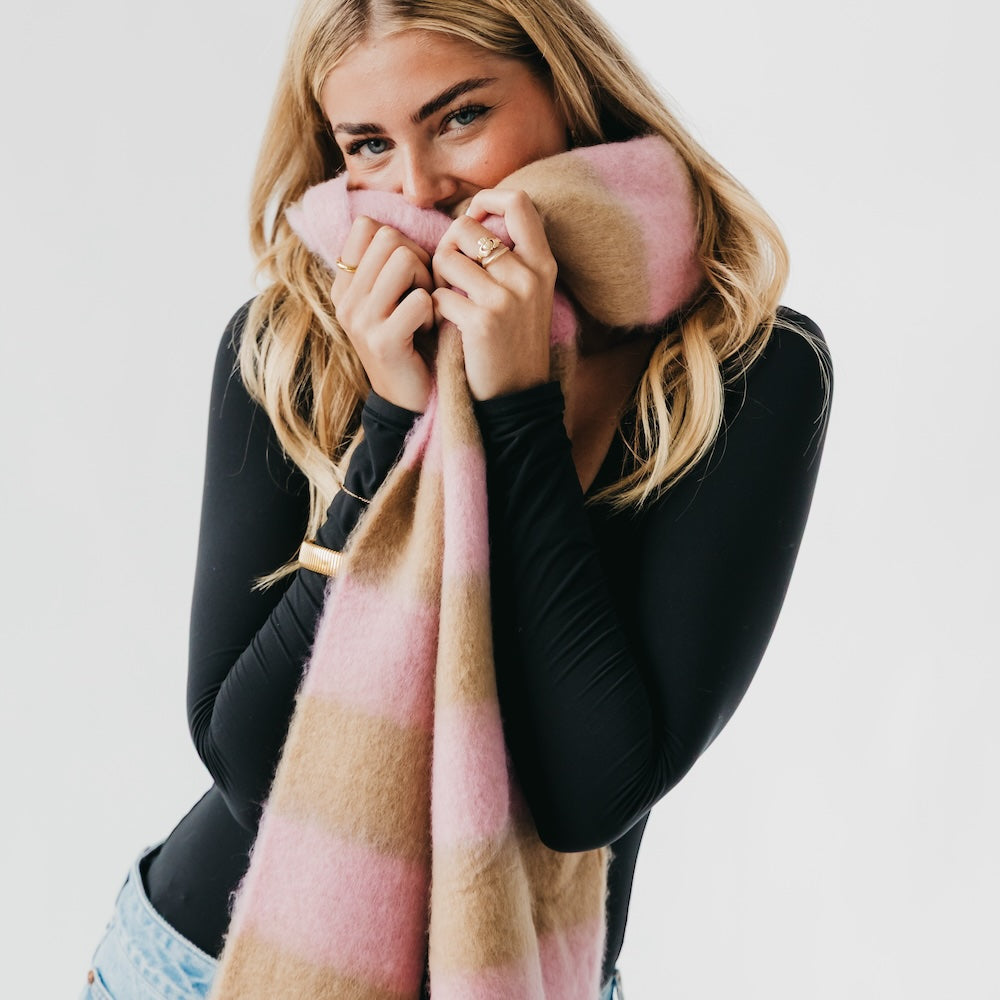 Woman holding a pink and brown plaid blanket against a plain background
