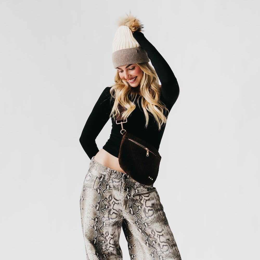 Woman wearing a black long-sleeve top, patterned pants, and a beanie with a white background