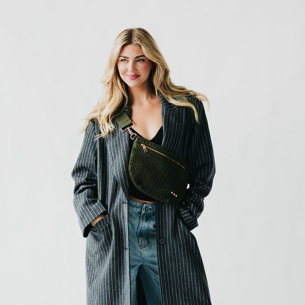Woman wearing a long coat and holding a green bag against a plain background