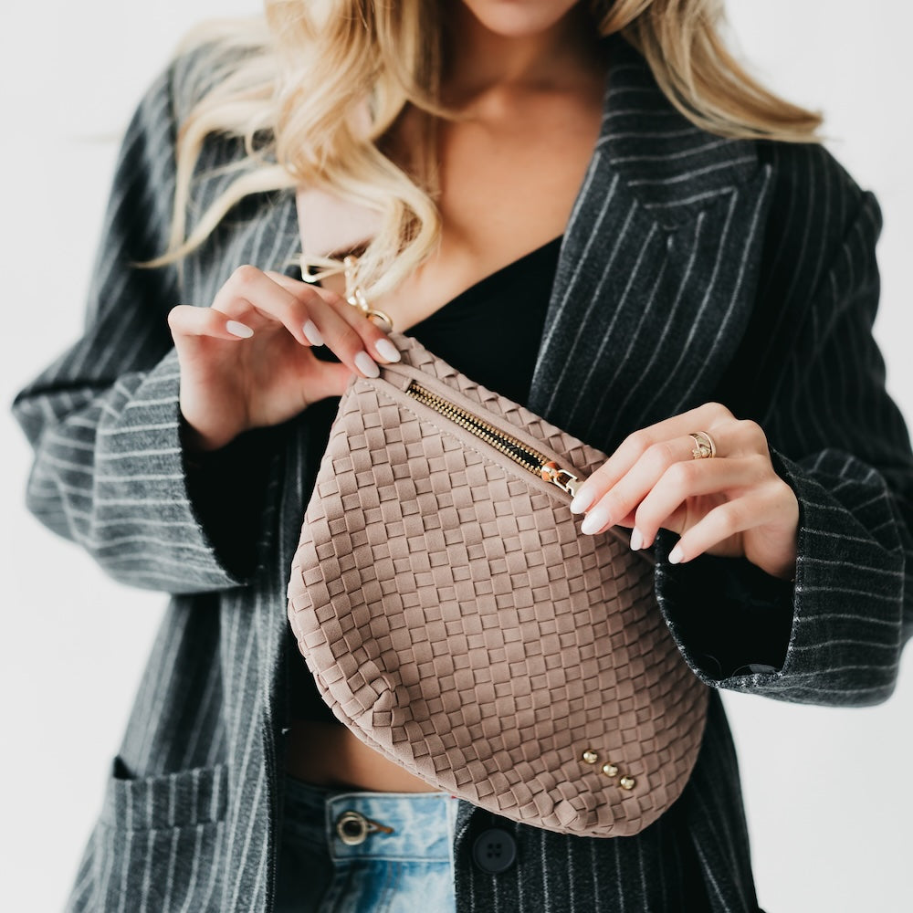 Person holding a woven beige handbag with a plain background