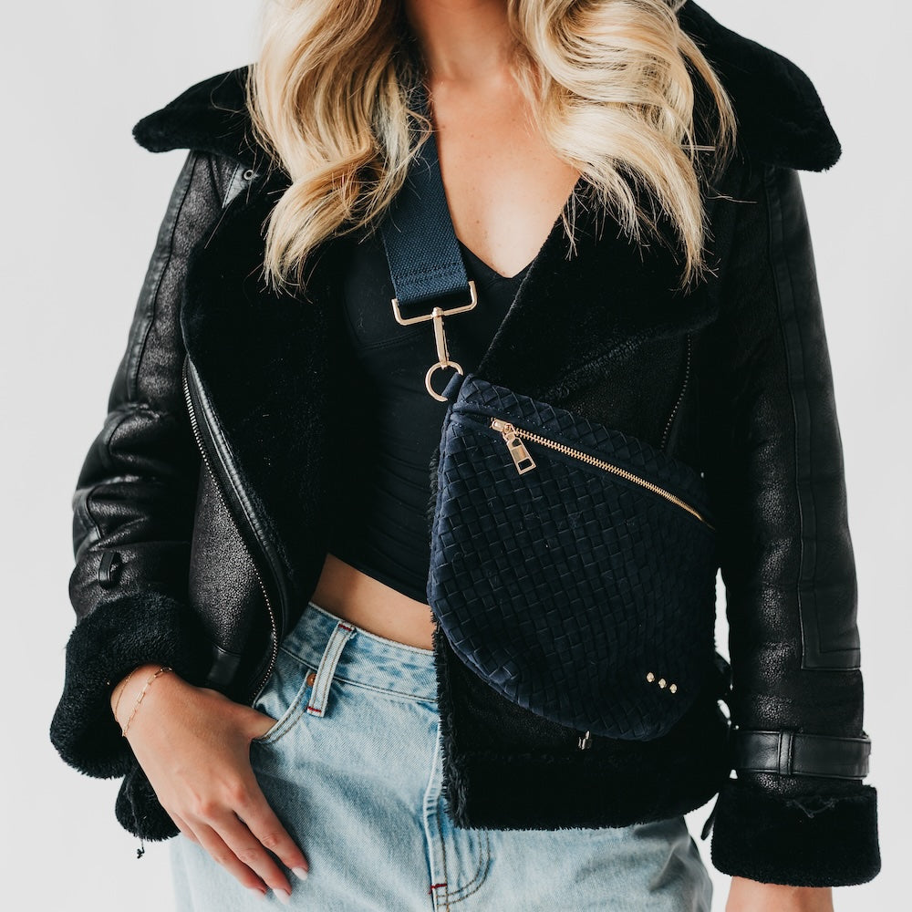 Person wearing a black leather jacket and holding a navy blue textured bag against a light background