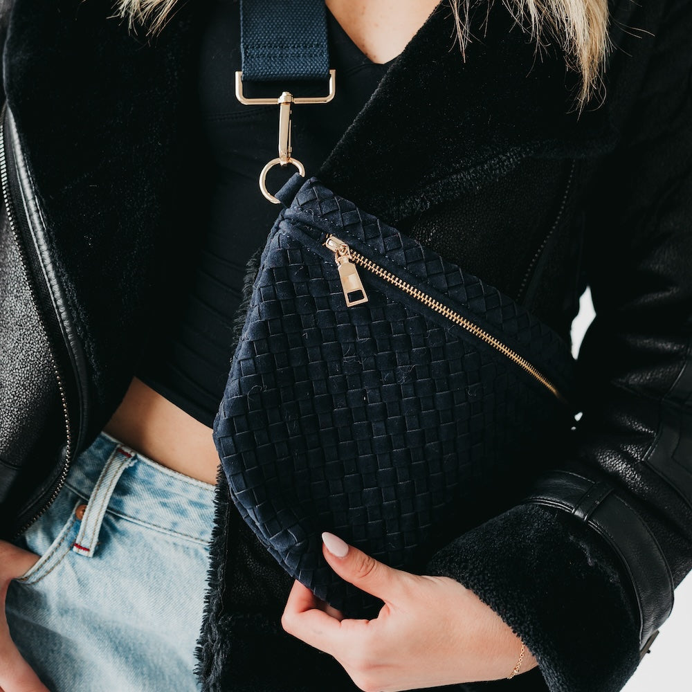 Person holding a black textured bag with gold zipper and strap.