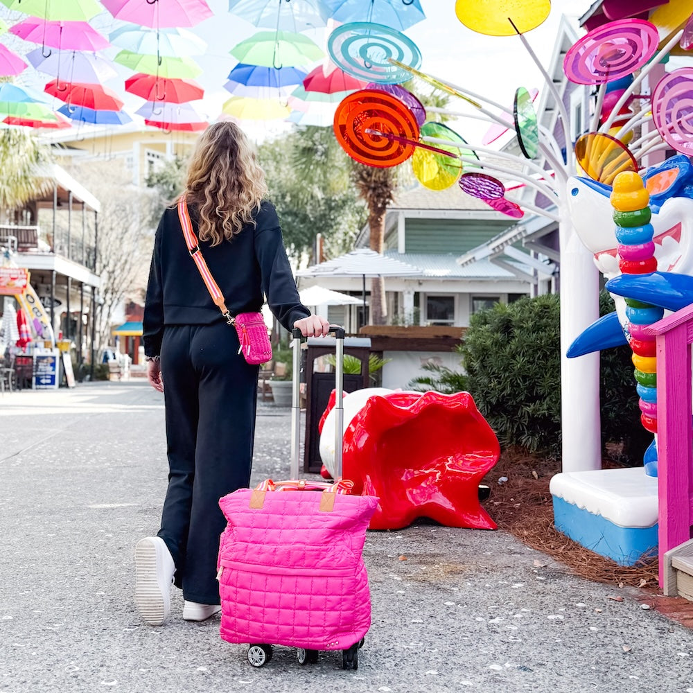 Woman with a pink suitcase walking under colorful umbrellas in a park-like setting.