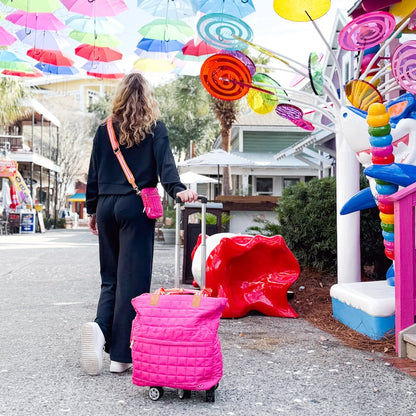 Woman with a pink suitcase walking under colorful umbrellas in a park-like setting.