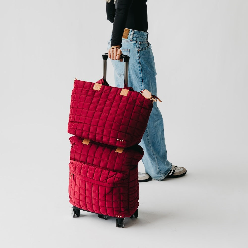 Person holding a stack of red quilted suitcases on a plain background