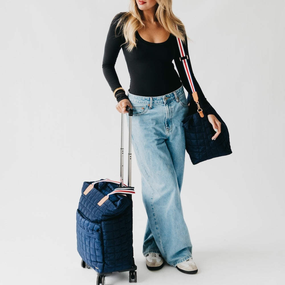 Woman holding a navy blue suitcase and handbag on a white background