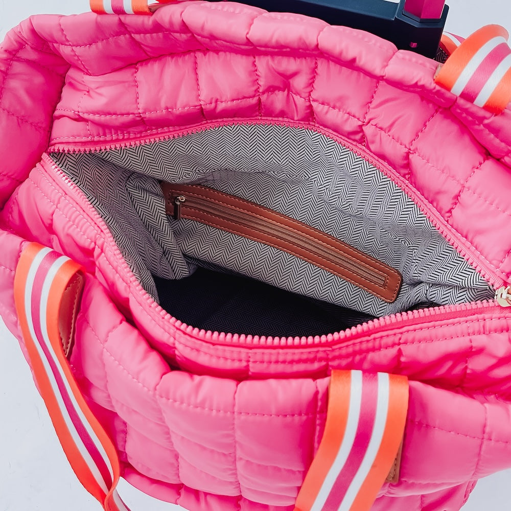 Close-up of a pink quilted bag with orange and white accents on a light gray background
