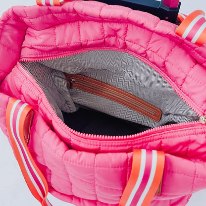 Close-up of a pink quilted bag with orange and white accents on a light gray background