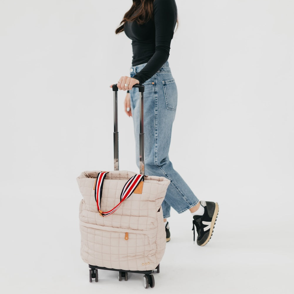 Person pulling a beige quilted rolling bag with a striped handle on a white background