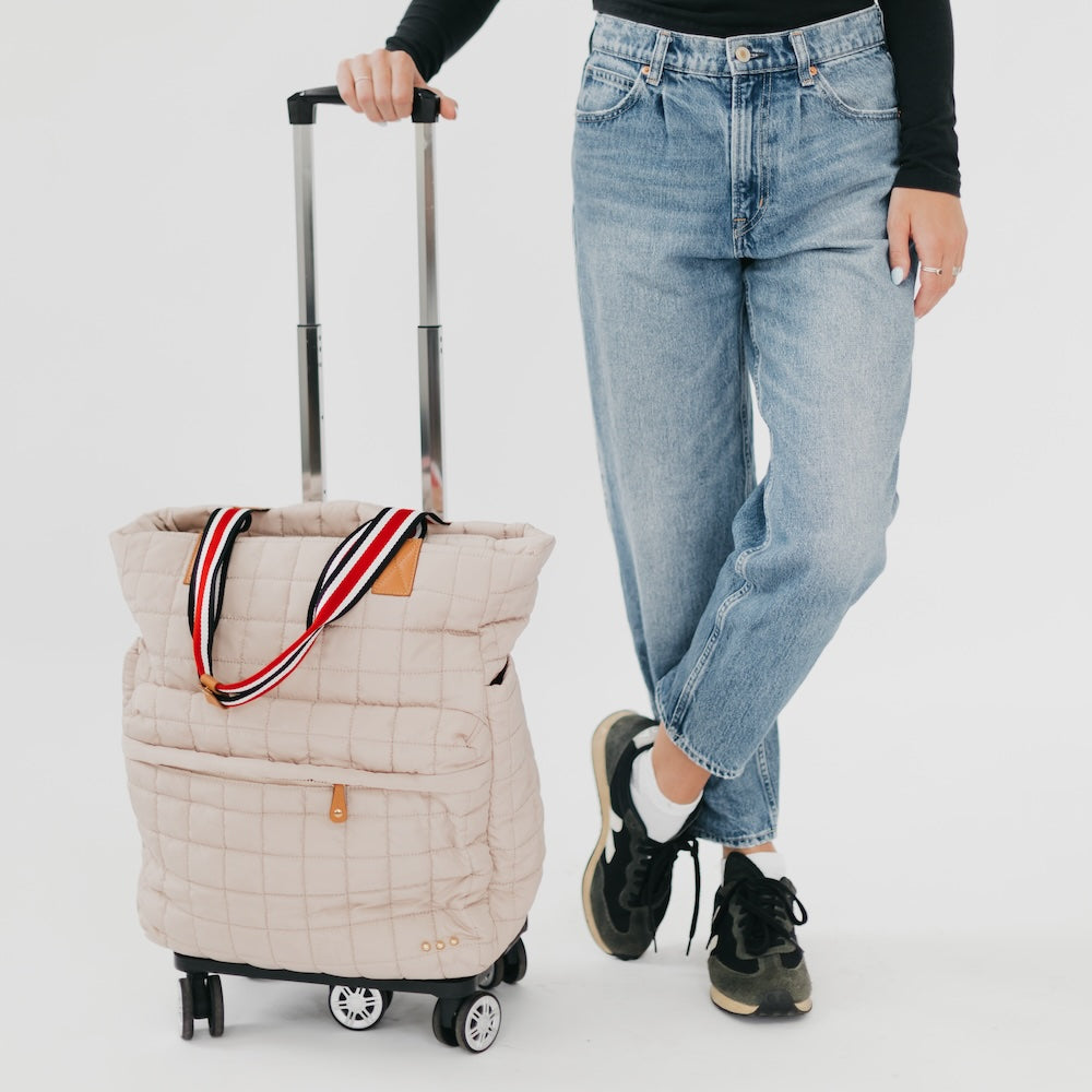 Person holding a beige quilted bag with wheels on a white background