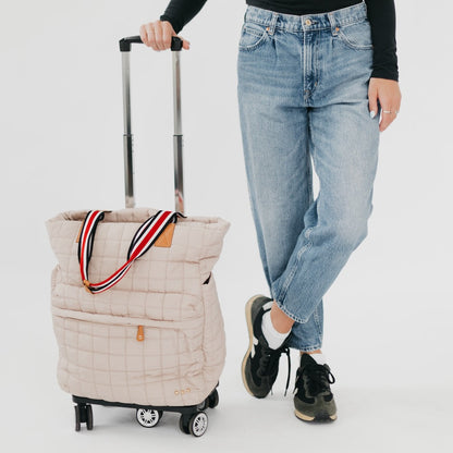 Person holding a beige quilted bag with wheels on a white background
