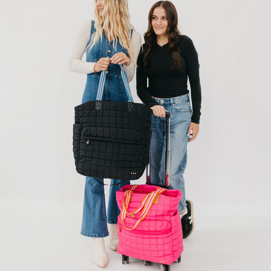 Two women holding a black quilted bag and a pink rolling bag against a white background