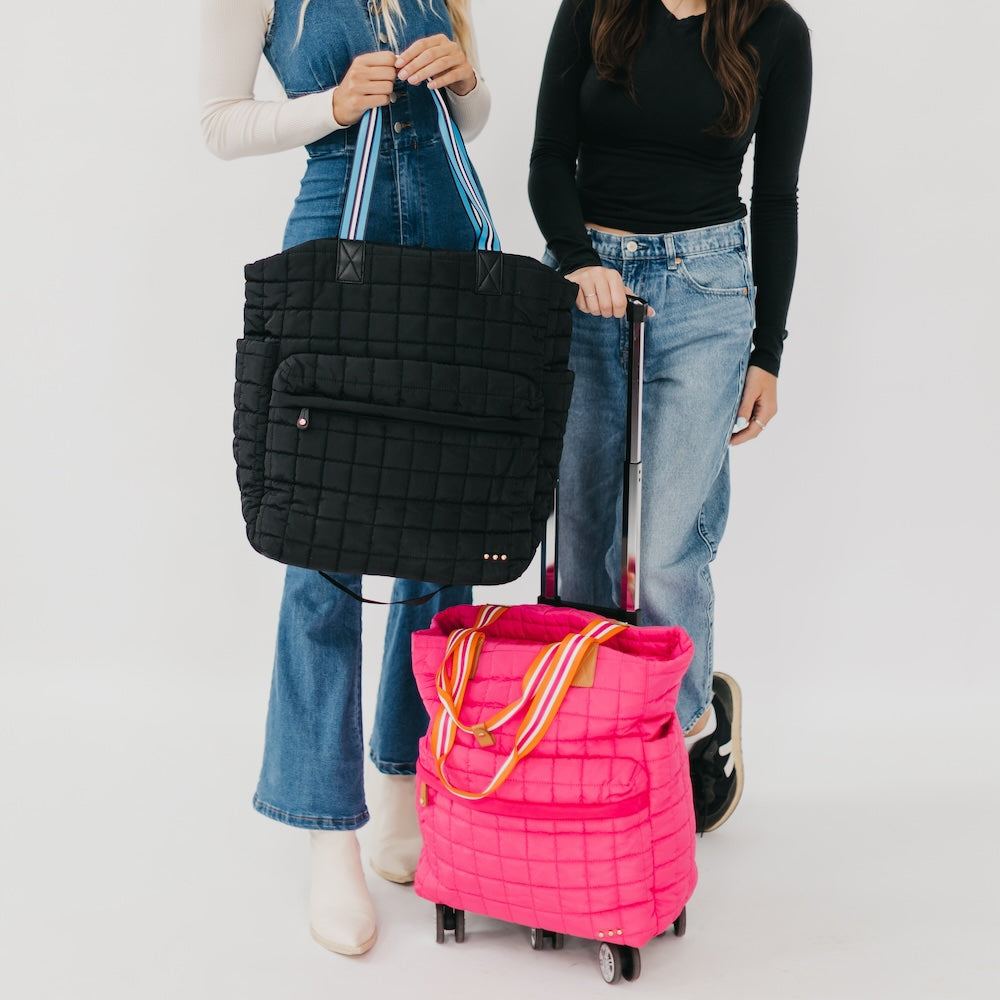 Two people holding a black quilted bag and a pink rolling suitcase on a white background