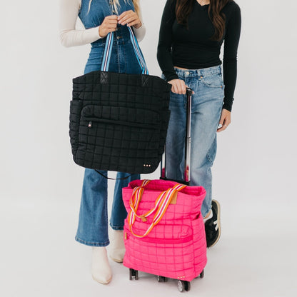 Two people holding a black quilted bag and a pink rolling suitcase on a white background