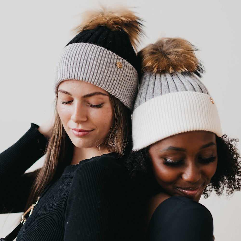 Two women wearing beanies with pom-poms against a plain background