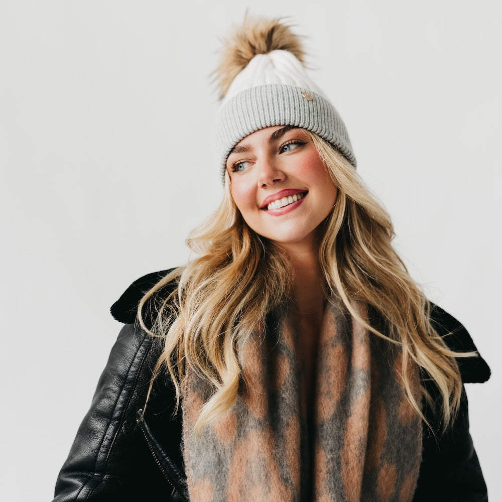 Woman wearing a beanie with a pom-pom and a scarf on a plain background