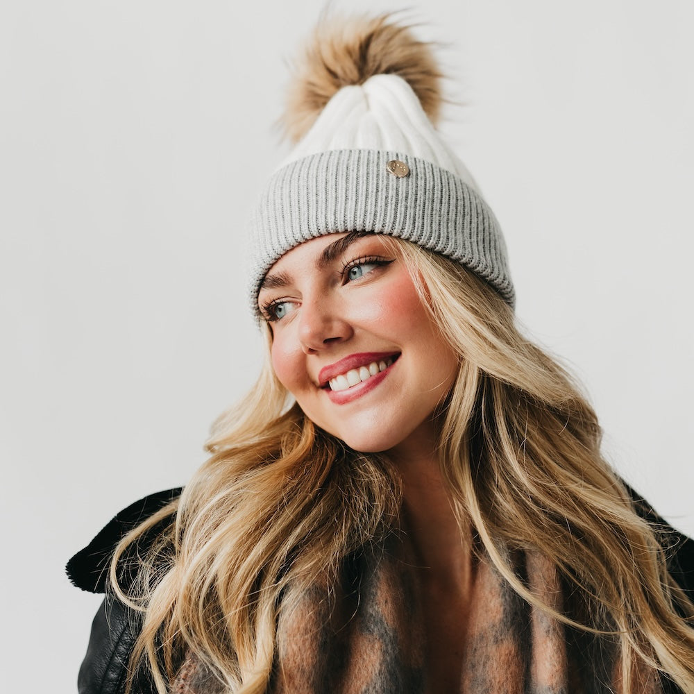 Woman wearing a gray beanie with a pom-pom on a plain background