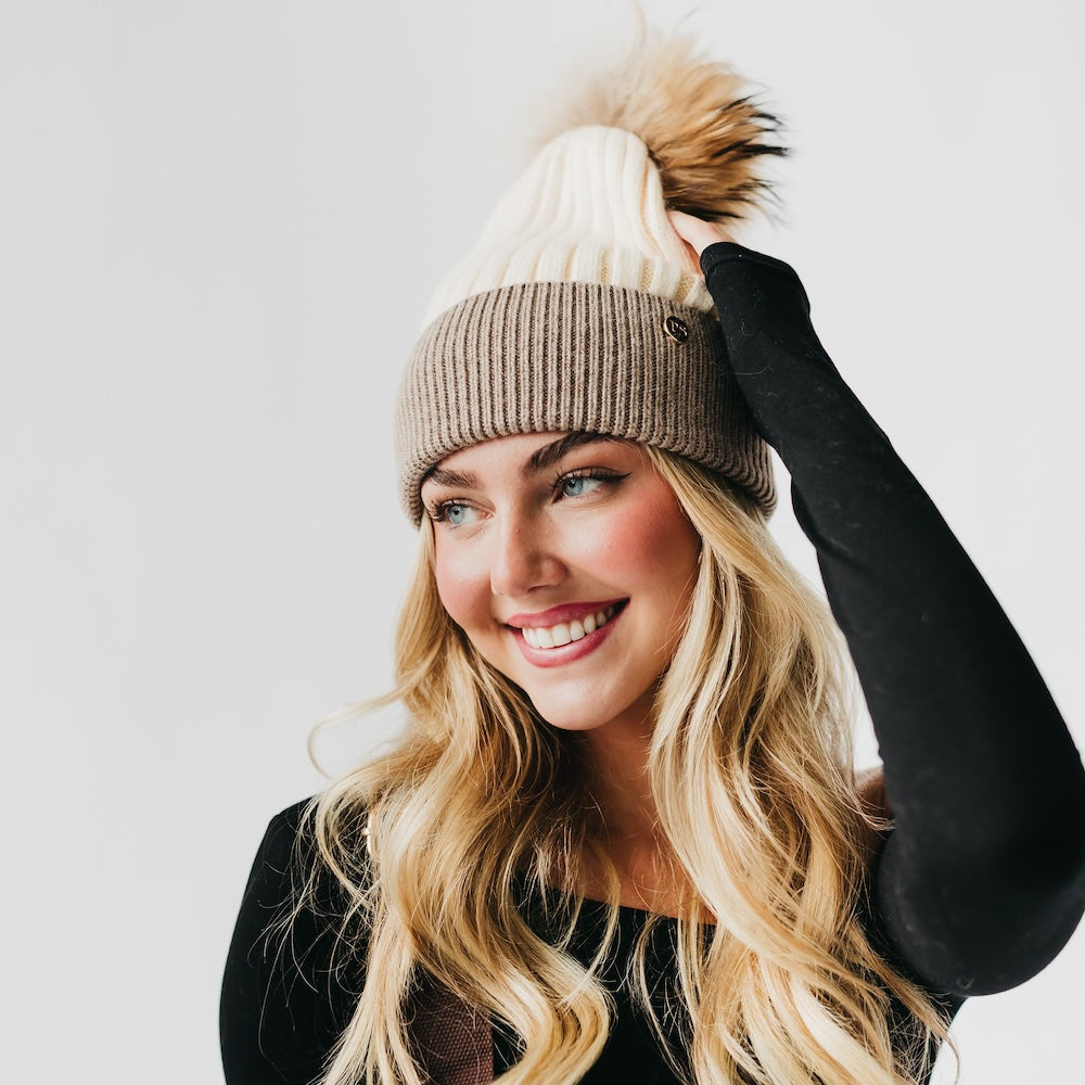 Woman wearing a beige knit beanie with a pom-pom on a white background