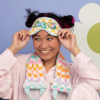 Person wearing a colorful checkered eye mask with text, smiling against a light blue background.