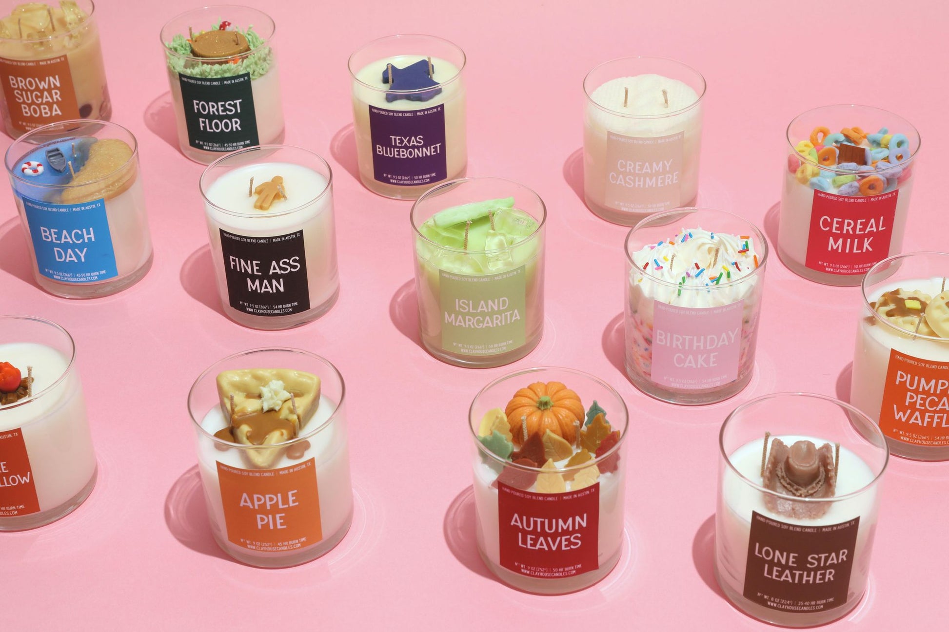 Assorted candles in glass jars with visible labels on a pink background