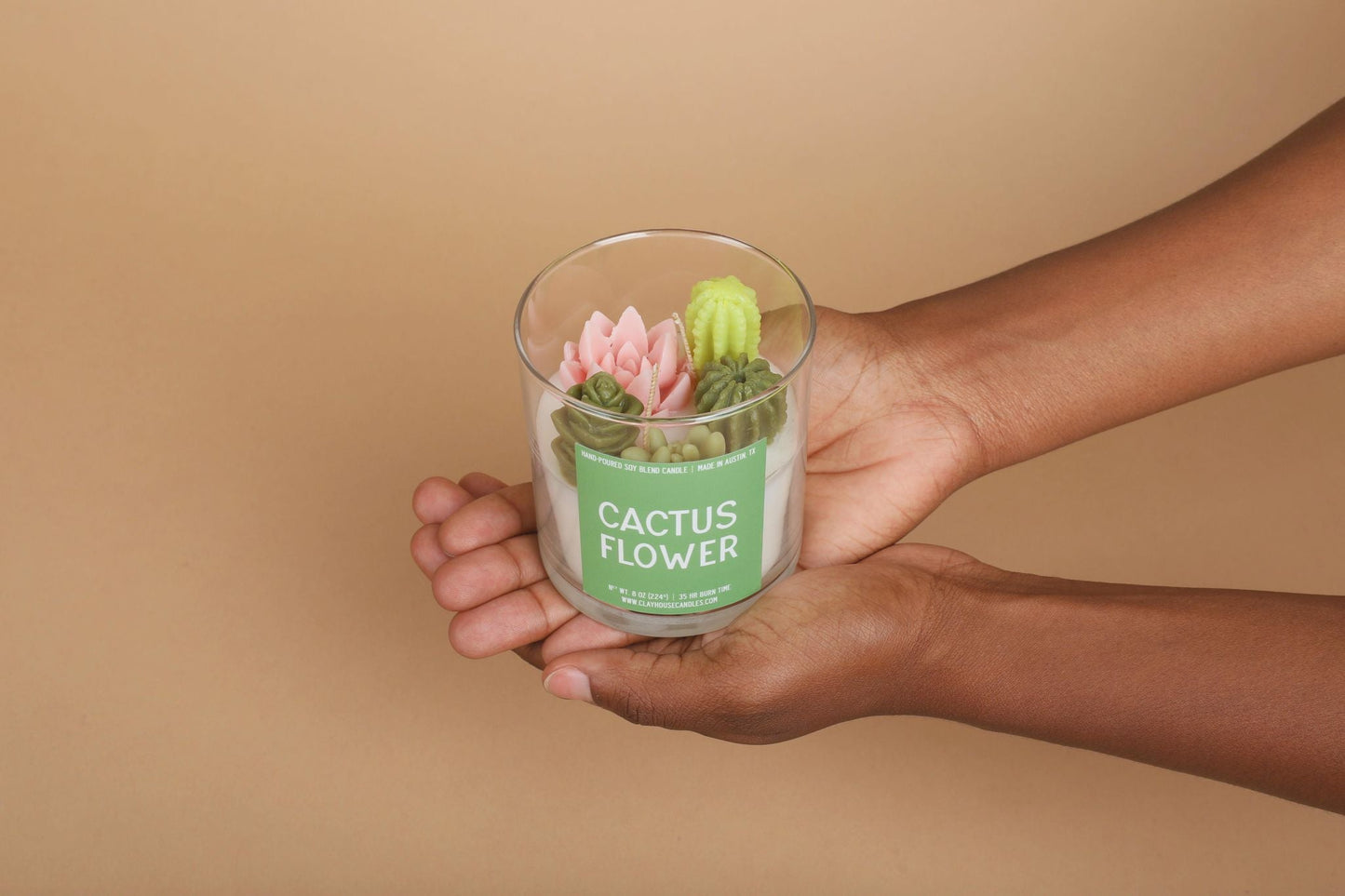 Hand holding a glass container with a cactus flower decoration against a beige background