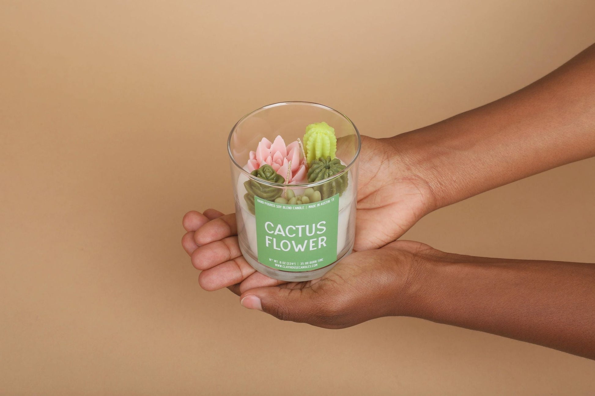 Hand holding a glass container with a cactus flower decoration against a beige background