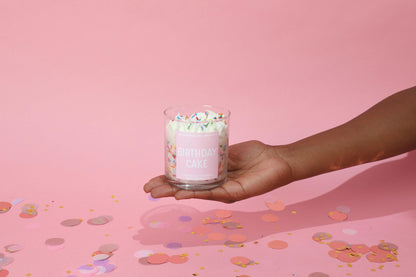 Hand holding a pink birthday cake candle with sprinkles against a pink background