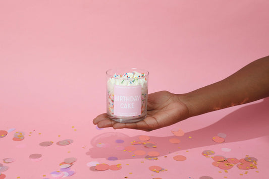 Hand holding a pink birthday cake candle with sprinkles against a pink background