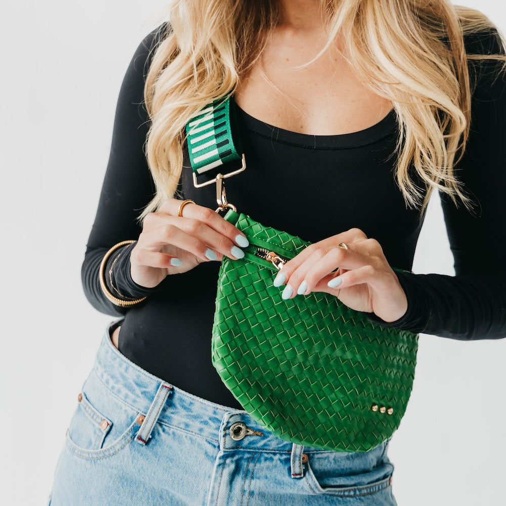 Person holding a green woven bag with a striped strap against a plain background