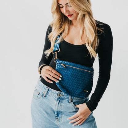 Woman holding a blue woven handbag against a plain background