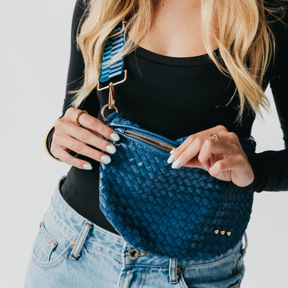Person holding a blue woven handbag with a plain background