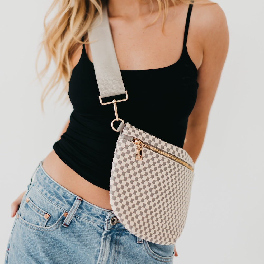 Person wearing a black top and blue jeans with a checkered fanny pack on a light background