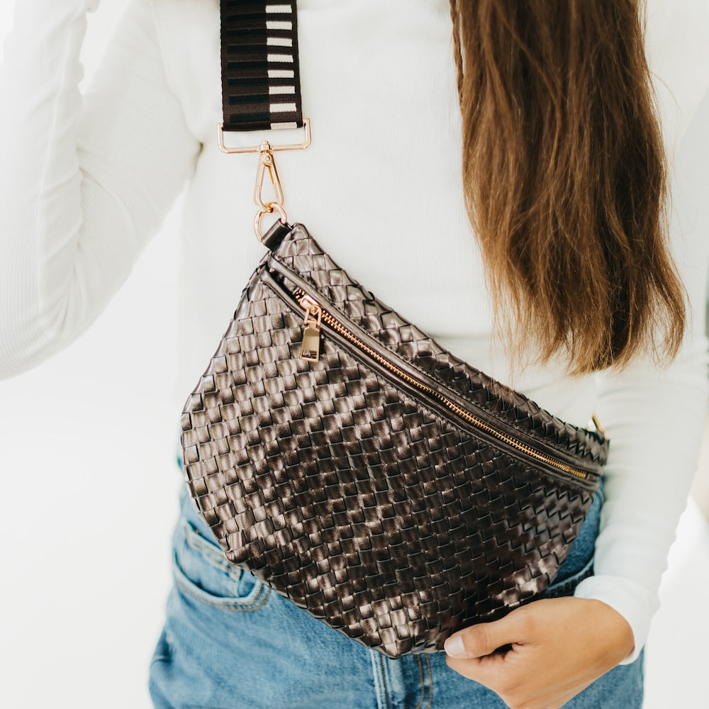 Person holding a woven handbag with a striped strap against a neutral background