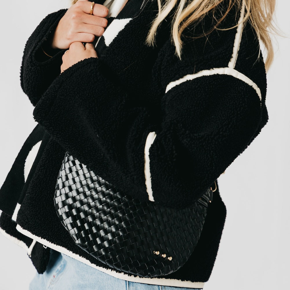 Black textured backpack with white accents held by a person against a light background