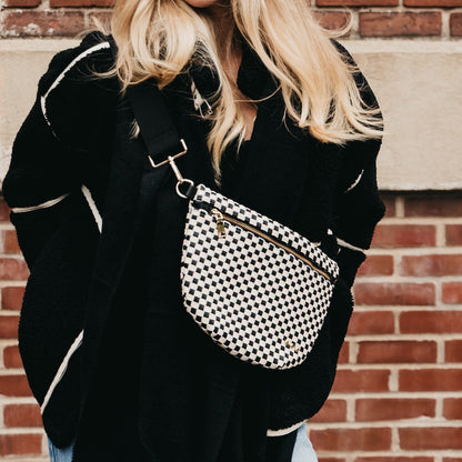 Person wearing a black coat with a black and white checkered bag against a brick wall.
