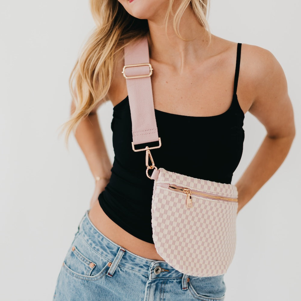 Woman wearing a beige woven fanny pack with a pink strap on a plain background