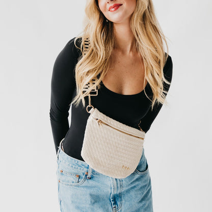 Woman wearing a beige woven belt bag with a gold zipper on a white background