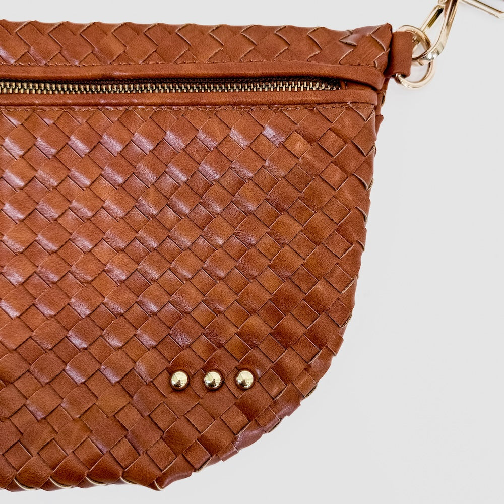 Brown woven handbag with gold zipper and hardware on a light gray background