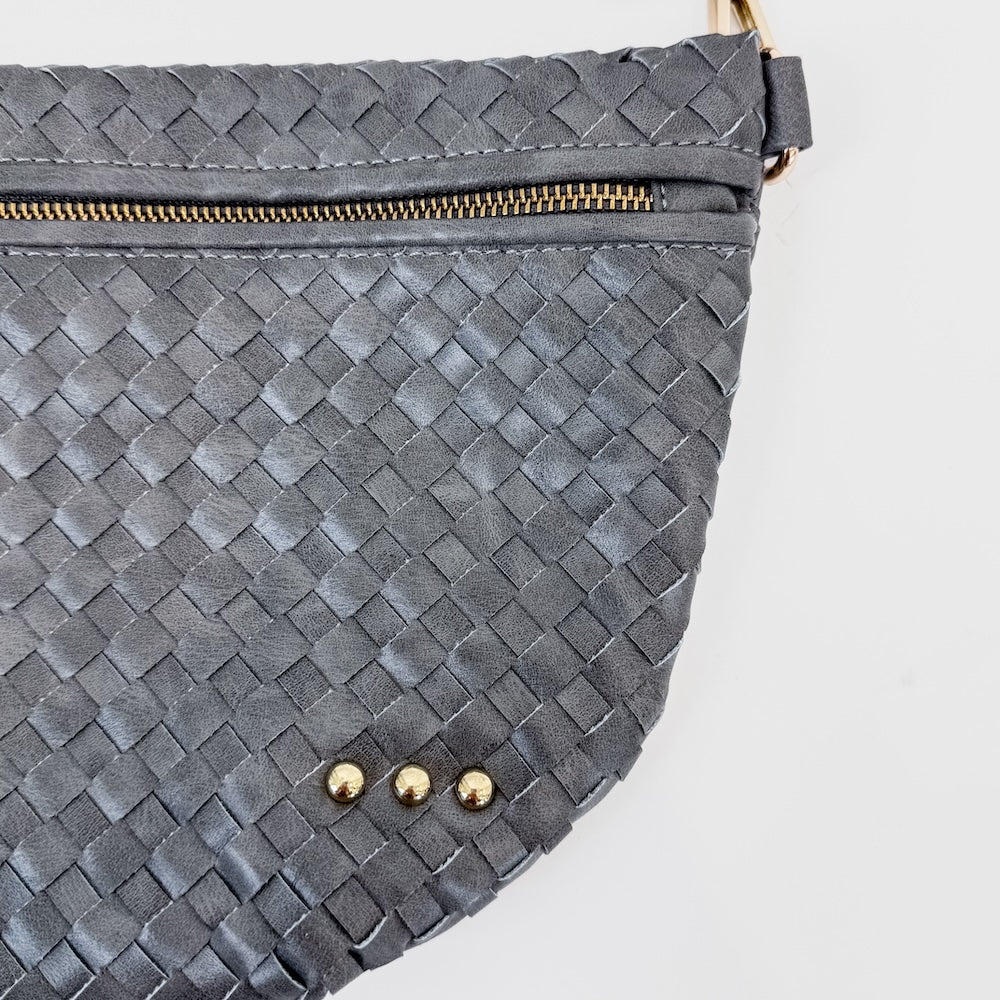 Gray woven handbag with gold zipper and studs on a light gray background